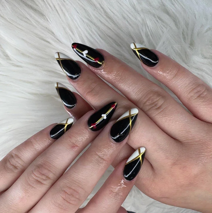 Black almond nails with gold lines and white accents by Muskoka Nails & Spa